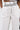 A close-up of a person wearing the BLANK SPACE HIGH WAIST PALAZZO PANT in white, featuring black piping details, a black waistband, and black trim along the zipper, pockets, and seams with a wide-leg silhouette.