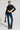 A person poses confidently in the trendy KNOCK YOU DOWN FITTED MOTO jacket with a cropped silhouette, blue flared jeans, and black platform boots, holding a small black patterned handbag. The plain white background highlights their fashionable look.