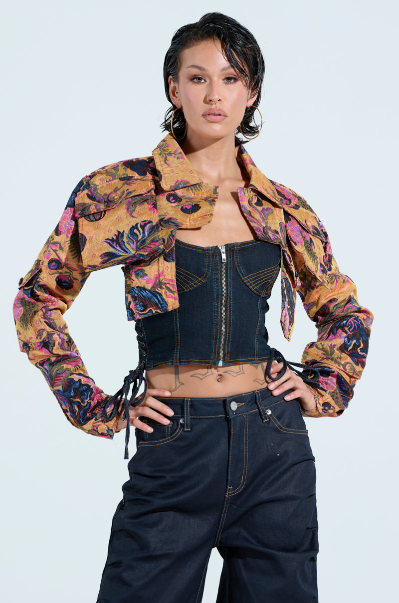 A person sports the ULTRA CROP CARGO BOMBER over a black strapless top with a zip front, matched with dark high-waisted jeans. They have short, wet-look hair and exude confidence against a plain backdrop.