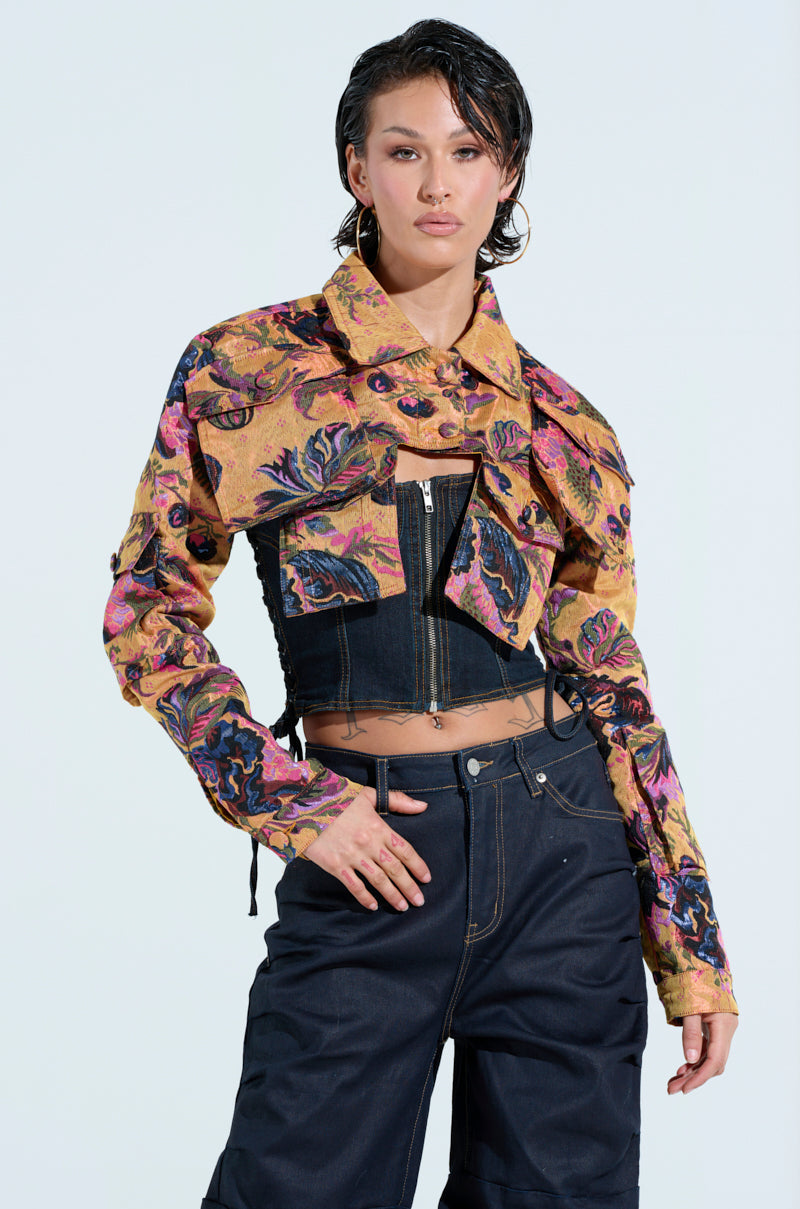 A person with short dark hair poses confidently against a light background, wearing the chic ULTRA CROP CARGO BOMBER over a dark corset top and black pants. The jacket's pink, purple, and yellow designs add a burst of color to their stylish ensemble.