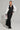 A person poses confidently in the sporty chic DO YOU MIND MAXI DRESS, featuring a long black and white zip-up design with stripes. They accessorize with layered necklaces, hoop earrings, and black heeled boots while holding a matching color-block design bag.