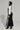 A person is dressed in the DO YOU MIND MAXI DRESS, a black and white ensemble with vertical stripes and a hood. They completed the look with black high-heeled ankle boots while posing against a plain gray background, glancing over their shoulder.