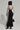 Against a plain gray background, someone exudes sporty chic vibes in the DO YOU MIND MAXI DRESS featuring a black and white color-block design with striped sleeves and an open back. They complete the look with a black hood, high-heeled boots, and a sleek black and white handbag.