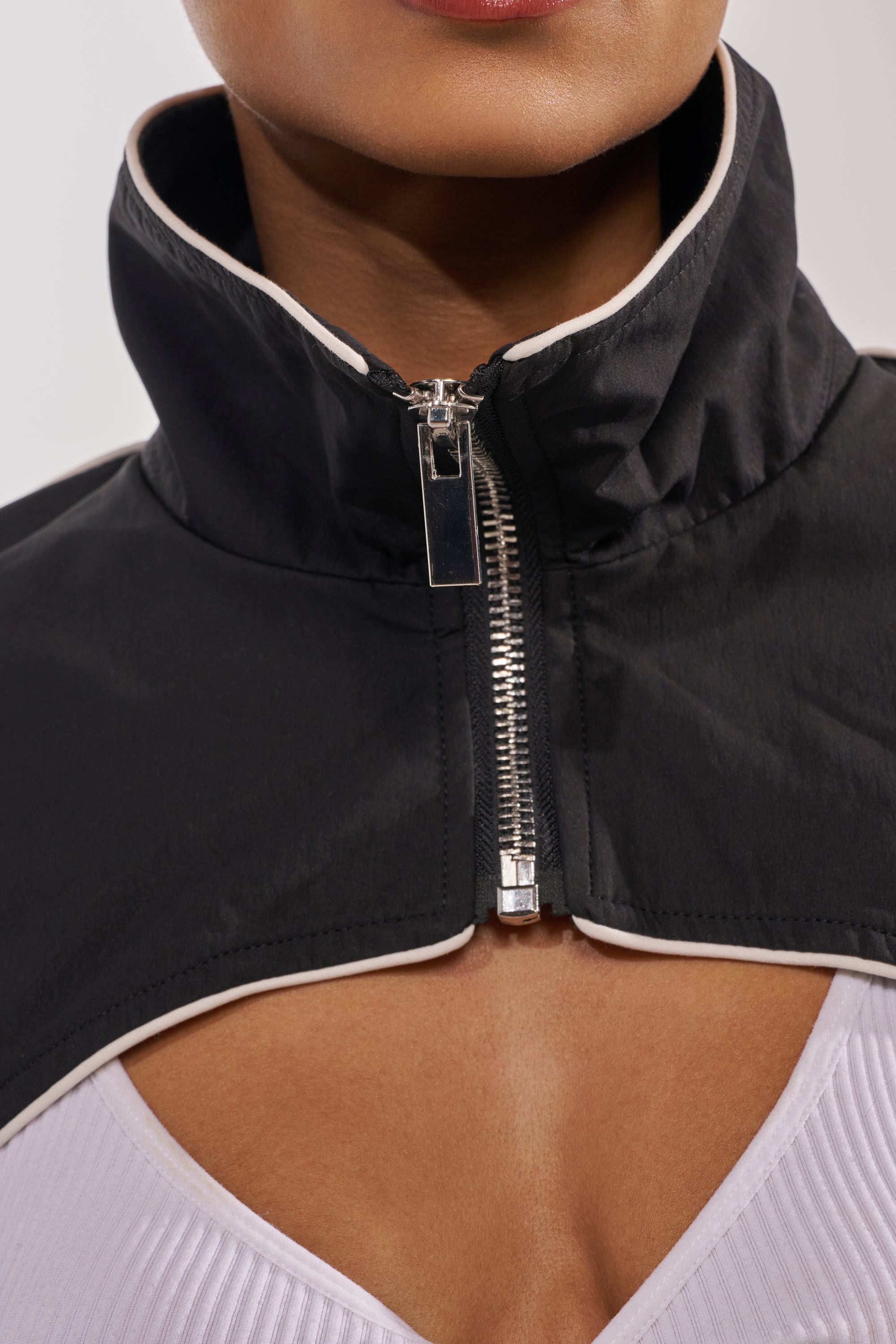 Close-up of a person wearing the NOW YOU SEE ME SPORTY BOLERO in black over a white ribbed top, with only their lower face, neck, and upper chest visible for a sleek athleisure look. 8