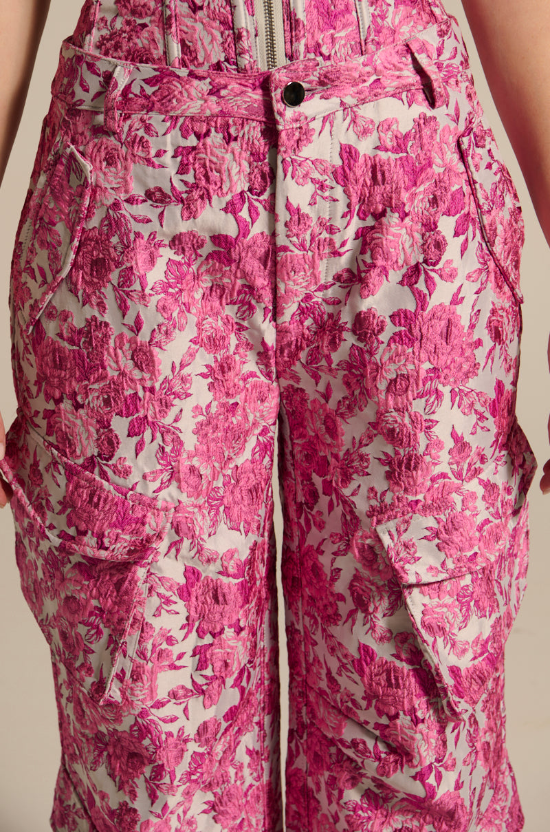 Close-up of a person in MILEY JACQUARD CARGO PANTS, showcasing a pink floral-patterned design with textured fabric, high-rise fit, wide legs, visible zipper, and pockets for both function and standout style. 9