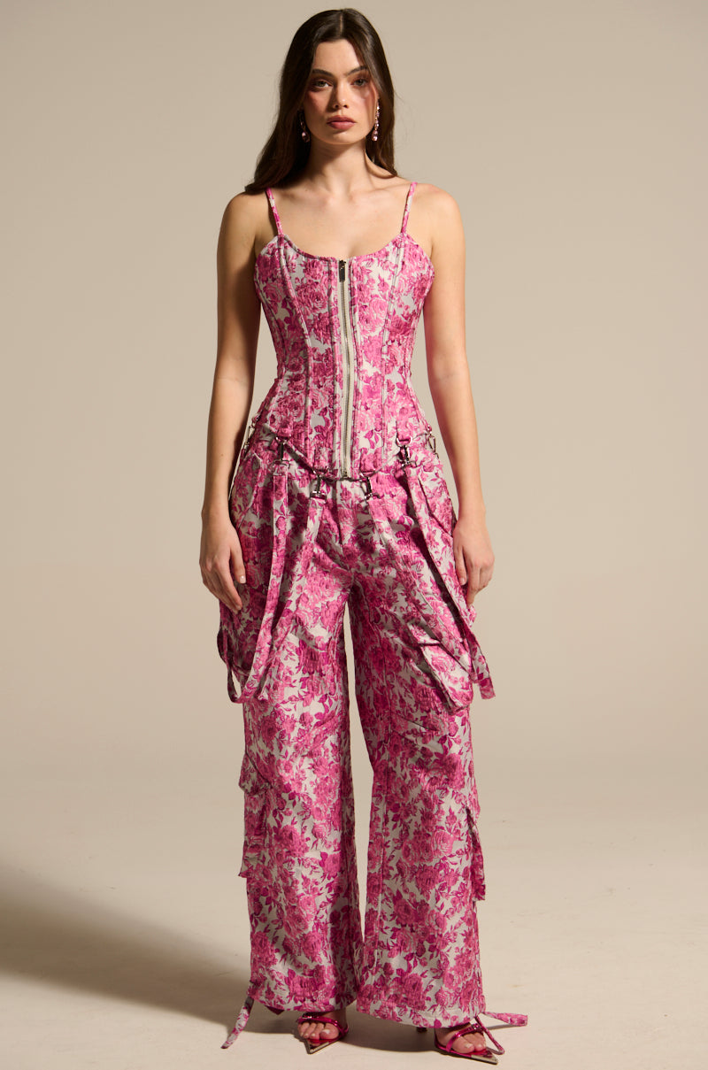 A person in a vibrant pink floral ensemble features a sleeveless corset top with a zipper and the MILEY JACQUARD CARGO PANTS. The plain, neutral background accentuates the lively outfit. 1