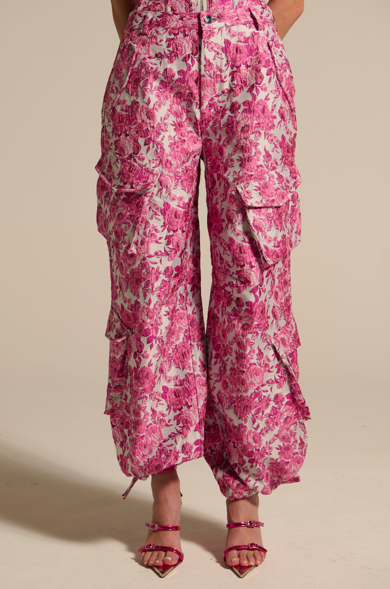Wearing MILEY JACQUARD CARGO PANTS in a pink floral print featuring multiple pockets and drawstring cuffs, the individual pairs these high-rise, wide-leg pants with pink strappy sandals set against a plain, neutral background. 3