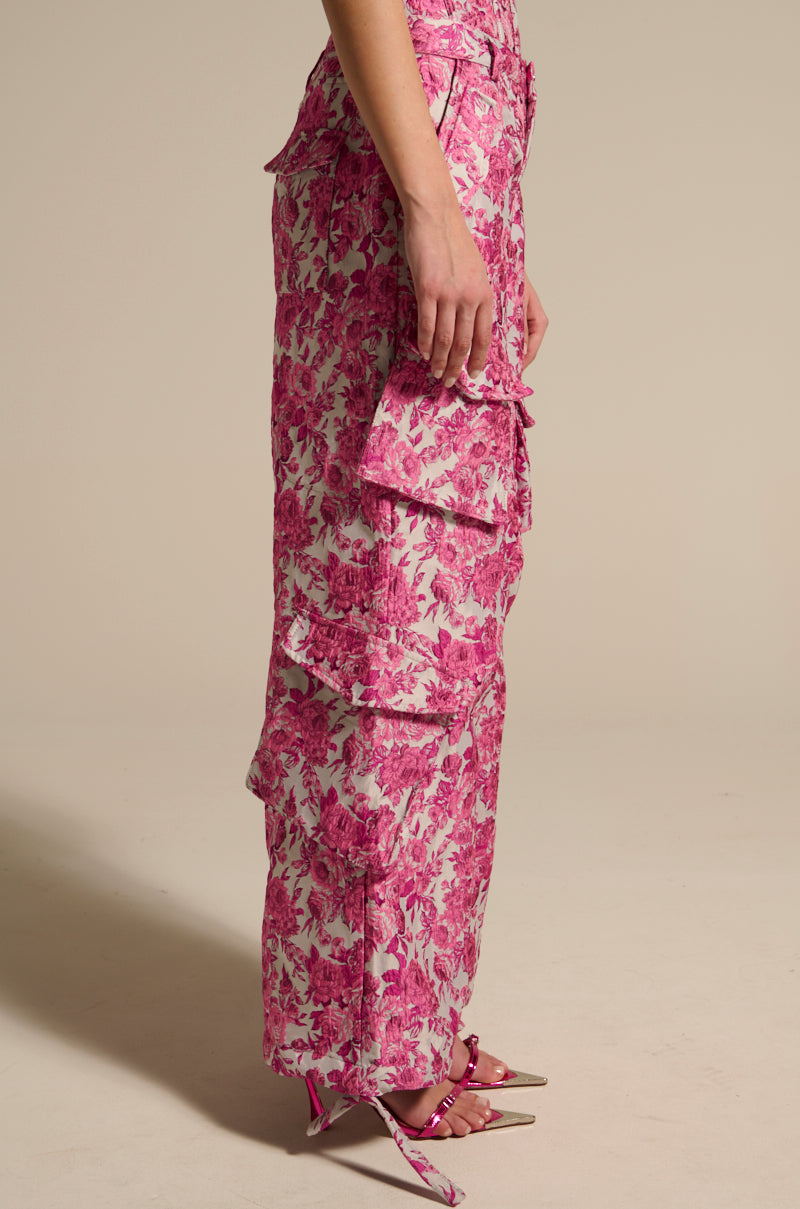 A person wears MILEY JACQUARD CARGO PANTS in pink floral jacquard with multiple pockets and tiers, paired with matching pink strappy heels. The image shows a side view against a plain beige background. 4