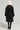 A person stands with their back to the camera, dressed in a STASSI FITTED PUFFER from AKIRA Label and a fluffy white hat. They're holding a small white handbag and wearing black knee-high boots with white patterns, highlighted by the coat's metallic front zipper closure.