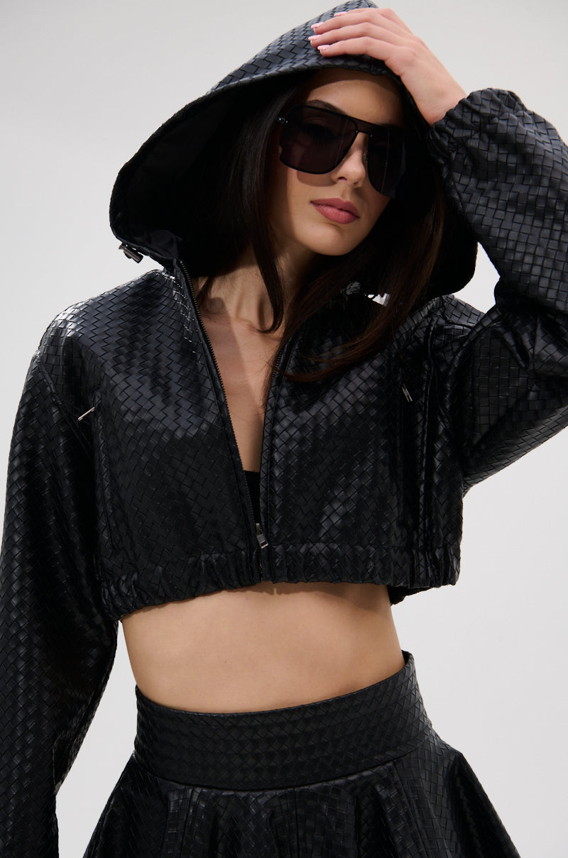 A woman poses against a plain light background, wearing the KYLIE HOODED BOMBER with a matching high-waisted skirt and large sunglasses, one hand touching her hood. 0