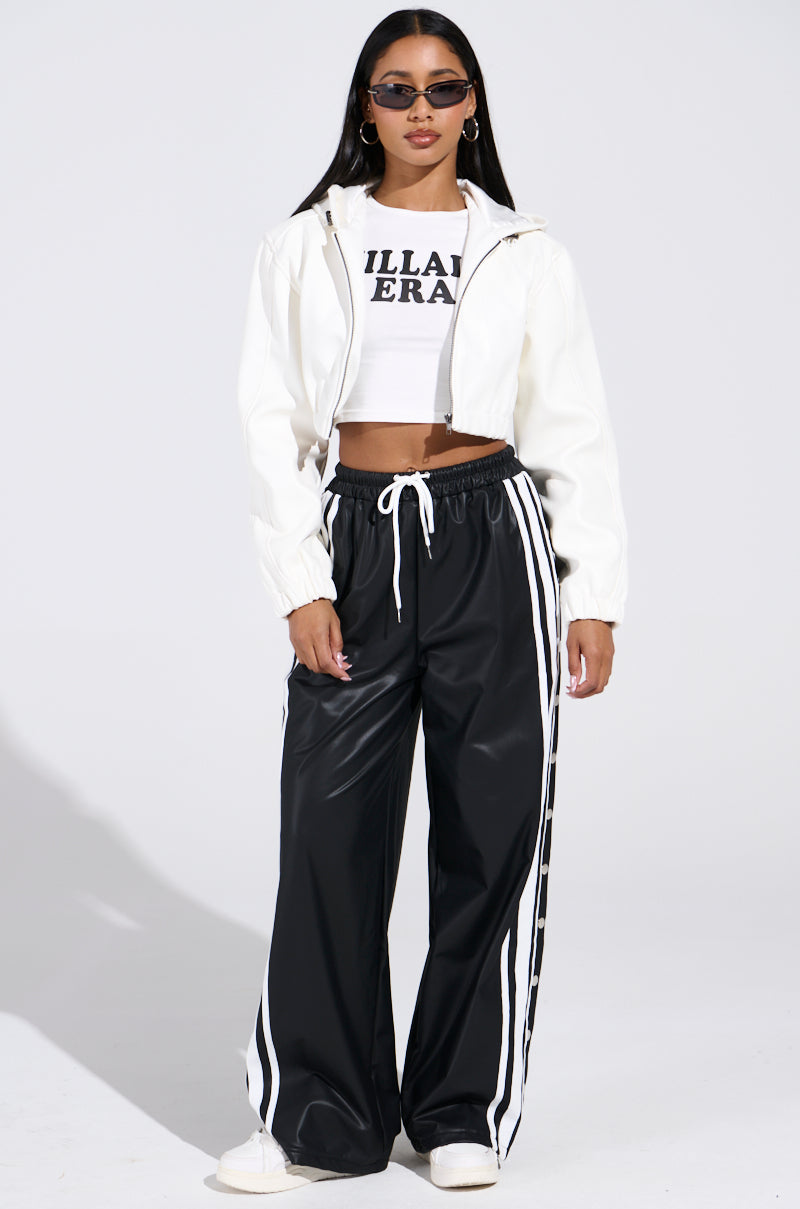 A person in sunglasses wears the "DEX HOODED BOMBER IN WHITE" over a text-adorned cropped top, paired with black track pants featuring white stripes. They stand casually against a neutral, well-lit background.