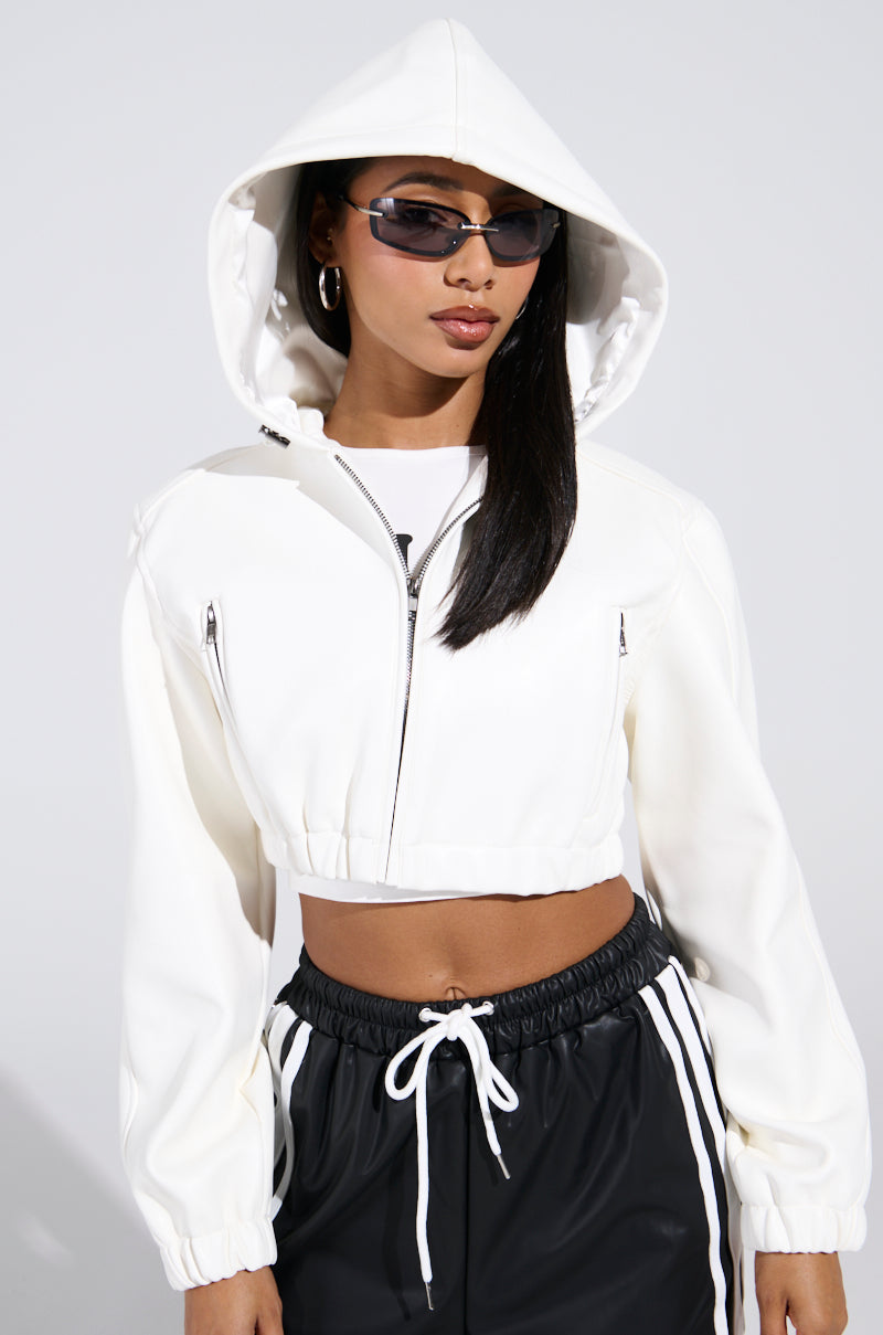 A person confidently wears the DEX HOODED BOMBER IN WHITE and black drawstring pants, accented by dark sunglasses and large hoop earrings. Their hood is up, set against a plain, light-colored background.