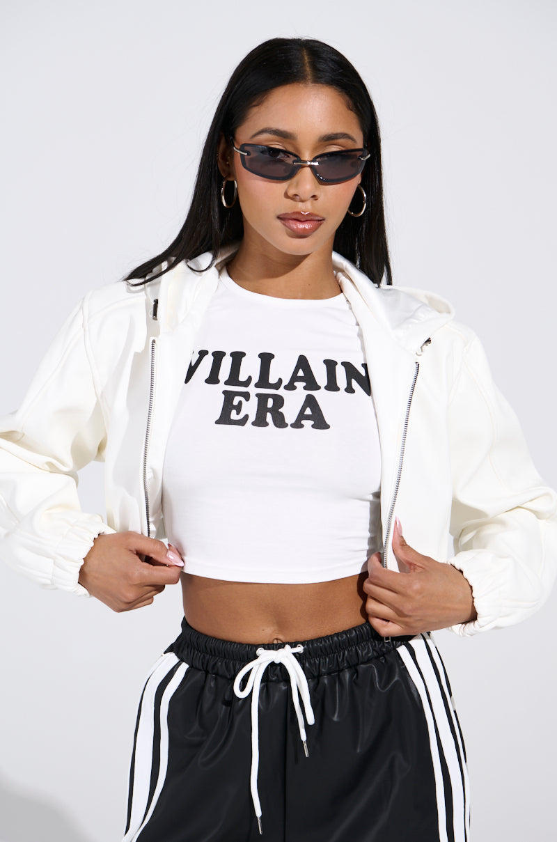 A person with long dark hair and sunglasses sports the DEX Hooded Bomber in White over a "VILLAIN ERA" crop top. Styled with striped black pants, this outfit completes a confident look against a plain backdrop.