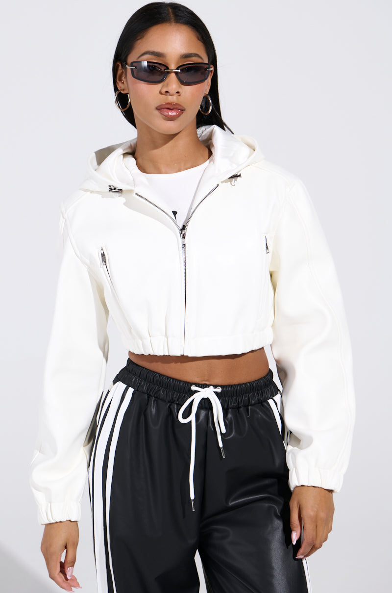 A person in a DEX Hooded Bomber in white and black track pants with white stripes poses confidently, sporting dark sunglasses and hands in faux leather pockets against a plain white background.