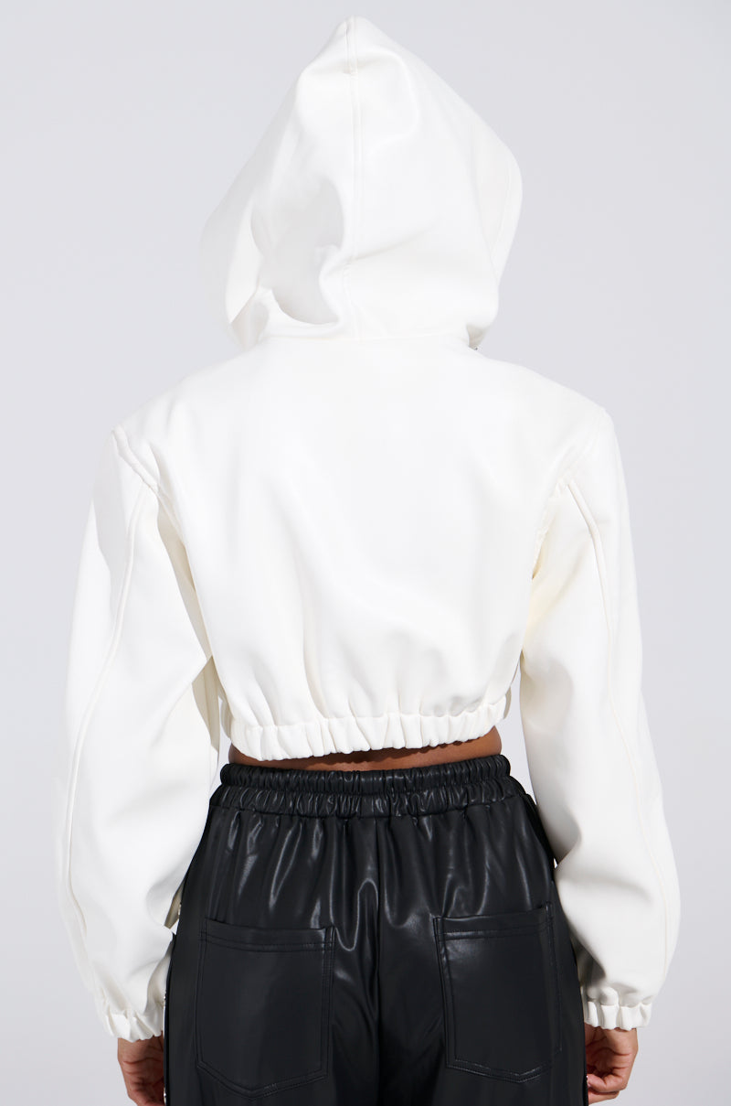 A person is seen from the back wearing the DEX HOODED BOMBER IN WHITE, showcasing its cropped silhouette and elastic waistband with the hood up. The elegant jacket pairs seamlessly with sleek black leather pants against a simple, light-colored backdrop.
