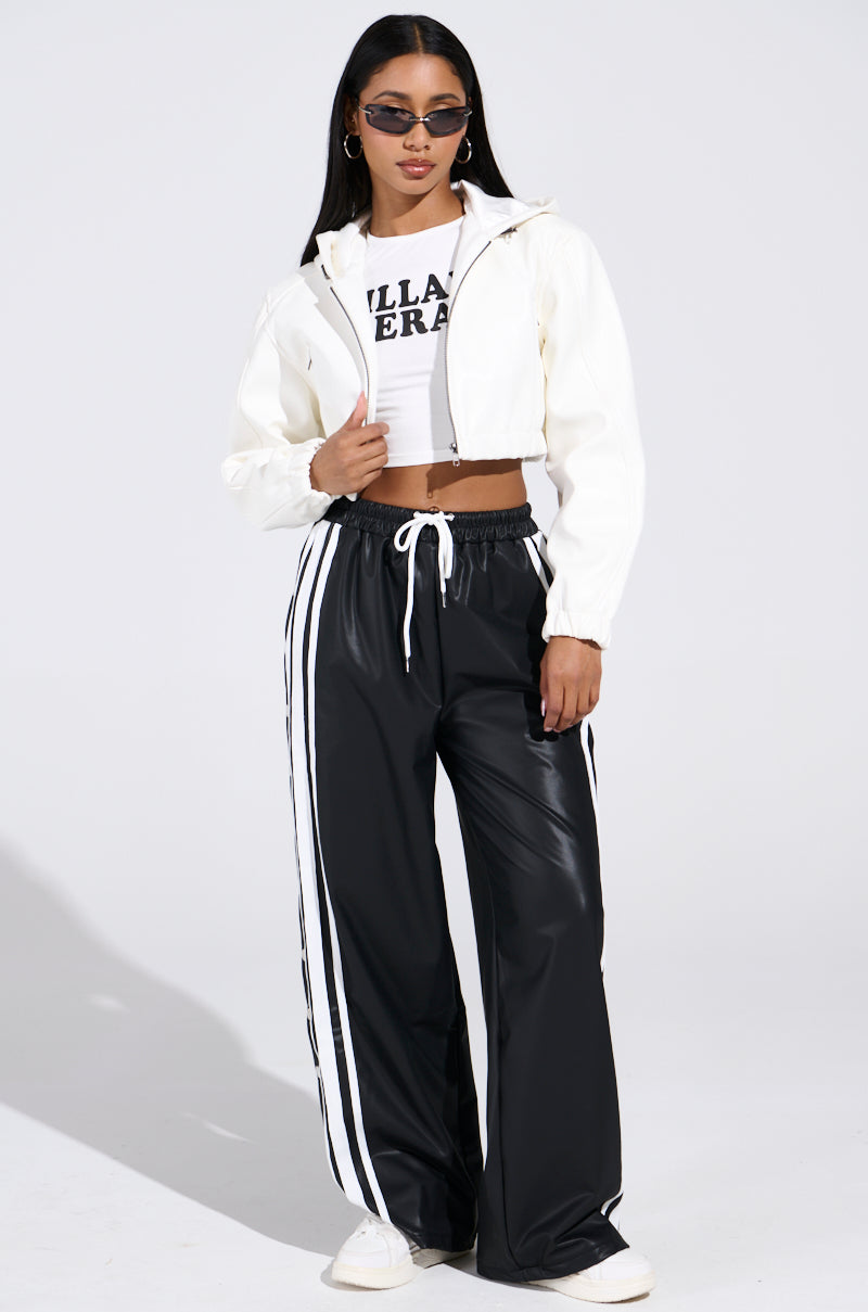 A person wearing sunglasses and a DEX Hooded Bomber in White over a graphic crop top. They're styled with black wide-legged pants featuring white stripes and white sneakers, posing confidently against a plain white backdrop that highlights the chic cropped silhouette.