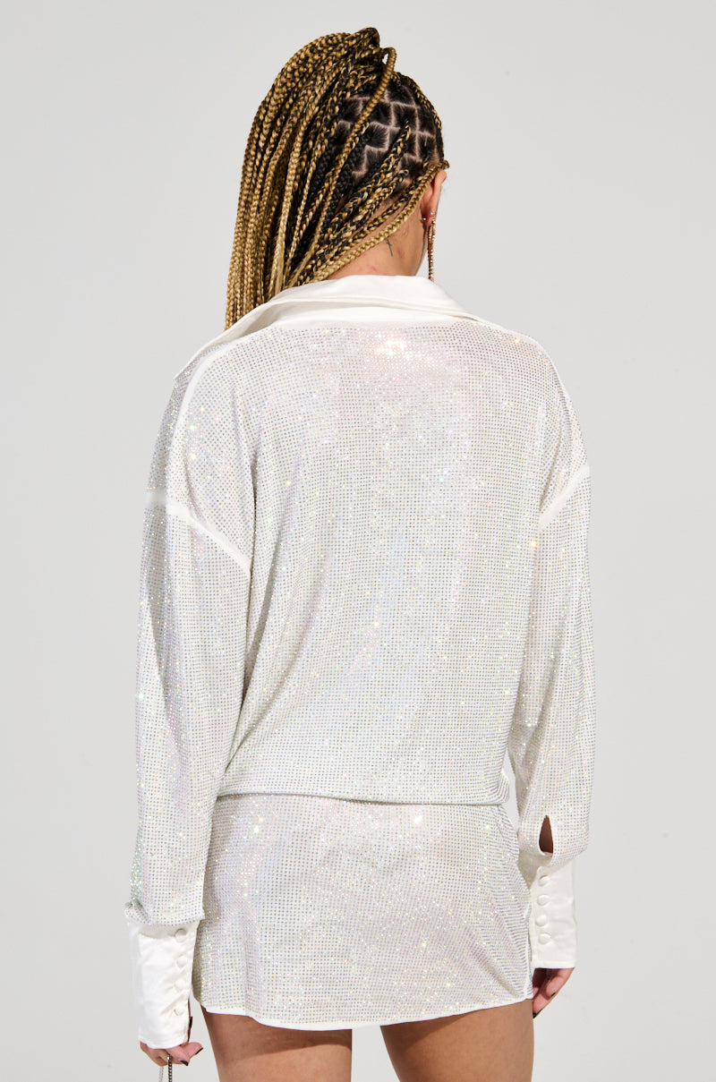 A person with braided hair is seen from the back, dressed in the LOGEN RHINESTONE MINI DRESS, a sparkling white ensemble that screams party look. The shimmering top with long sleeves and a collar pairs perfectly with matching short bottoms, while sequin embellishments add an extra touch of glamour against the plain background.