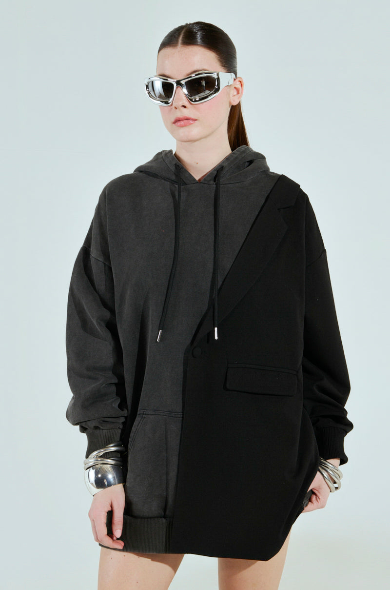 A person stands against a light background in a cotton-blend CASUAL BUSINESS SWEATSHIRT BLAZER MINI DRESS, seamlessly merging casual and formal style. They showcase sleek hair, large reflective sunglasses, and bold silver bracelets.