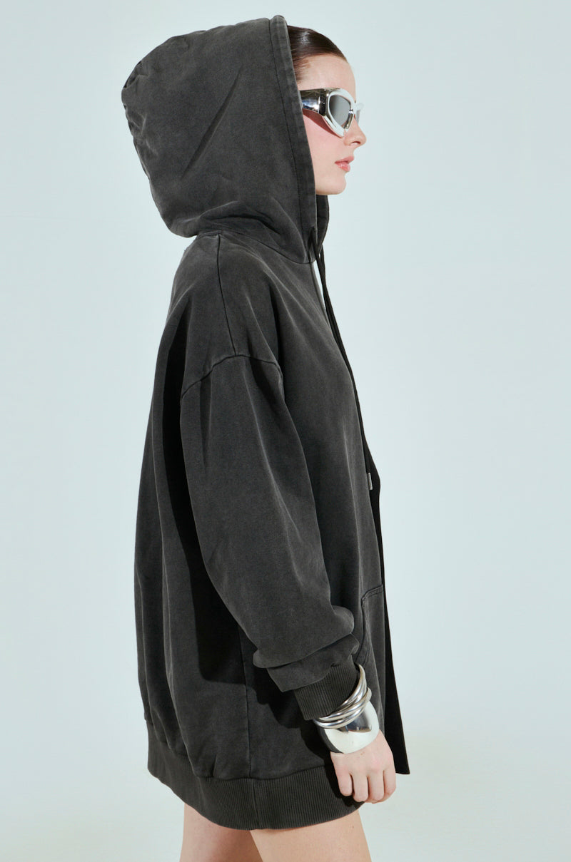 A person in a cotton-blend black CASUAL BUSINESS SWEATSHIRT BLAZER MINI DRESS, facing sideways, wears large sunglasses and bangles. The hood is up against a plain backdrop, effortlessly blending style with the dress's casual business vibe.