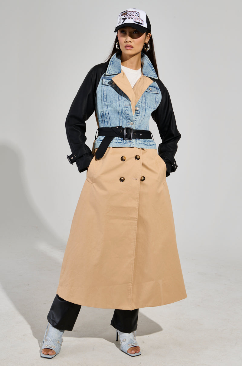 The CITY SLICKER MIXED MEDIA TRENCH pairs elegantly with a denim jacket layered over a beige base, flawlessly matched with black pants and open-toed heeled boots. Topped off with a patterned white cap, the outfit radiates confidence as the individual strikes a hands-in-pockets pose.