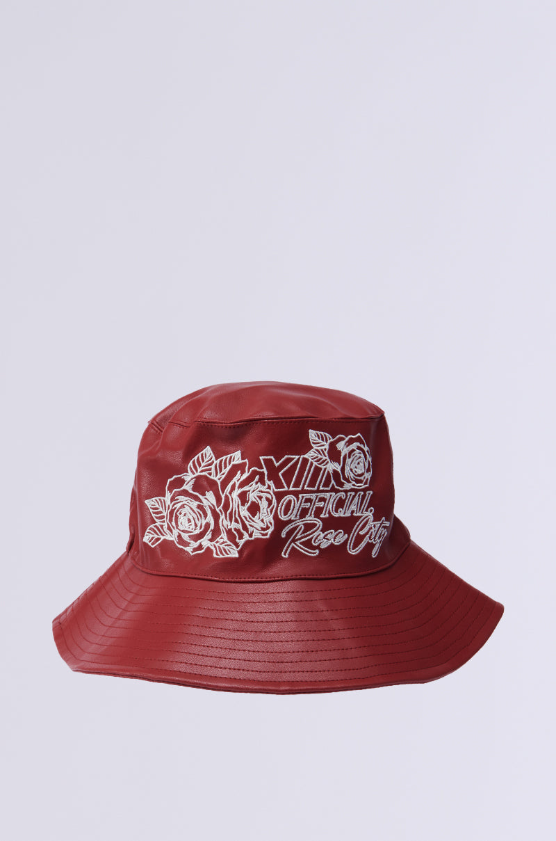A red ROSE CITY EMBROIDERED PU BUCKET HAT with white rose illustrations and "Official Rose City" text adorns the front, featuring a wide, downward-sloping brim against a plain, light background. 2