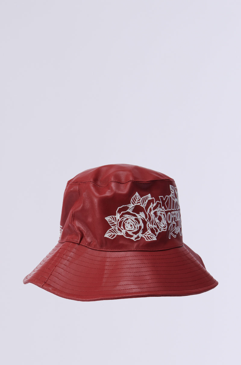 The ROSE CITY EMBROIDERED PU BUCKET HAT features a glossy faux leather with red bucket style, adorned with white rose outlines and the phrase "KILLING ORDINARY" in stylized lettering, offering a slightly worn-in look. 3