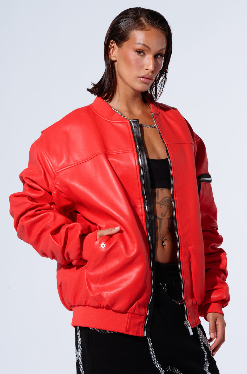 A person with wet hair is sporting the STORMY OVERSIZED BOMBER in a vibrant red faux leather over a black crop top, showcasing a torso tattoo. They pose confidently with one hand in the jacket pocket against a plain white background.