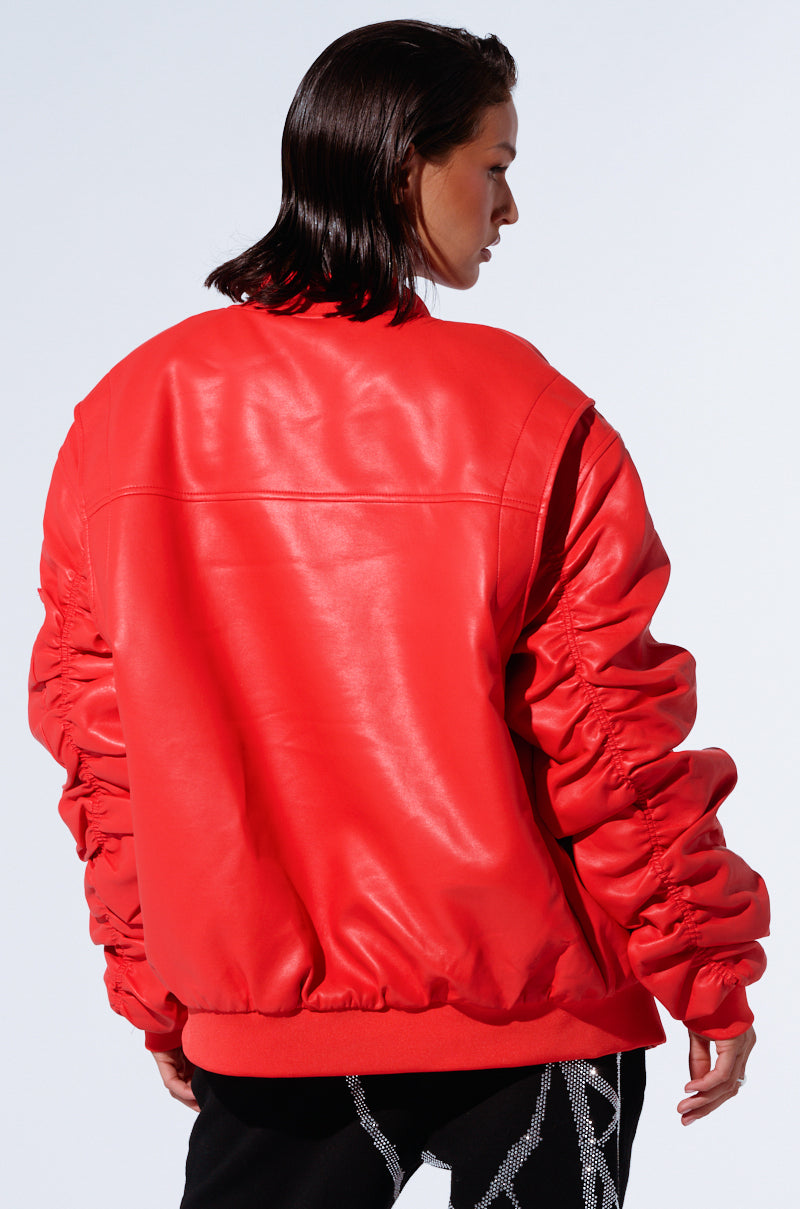 A person with wet, slicked-back hair is wearing the STORMY OVERSIZED BOMBER, featuring bright red fabric and ruched sleeves. The oversized silhouette adds a bold touch as they face away from the camera, revealing the back and left side of their profile against a plain light blue background.