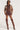 A stylish individual poses confidently in the AKIRA Label WISH ME LUCK EMBROIDERED MOTO jacket, a cropped brown faux leather piece adorned with letterman patchwork embroidery. They pair it with a maroon pinstriped mini skirt and matching top, tie, and high brown leather boots featuring intricate designs. Dark sunglasses complete the look.