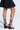 Sporting the AZALEA WANG ISAAK black wedge sandals with white crisscross back laces, three straps, and open toes against a plain, brightly lit background highlights their unique design and comfort cushion feature.