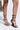 Close-up of a person wearing AZALEA WANG ISAAK Black With White Laces Wedge Sandals, holding a brown snakeskin-patterned handbag against a light grey background, with light pink polished toenails.
