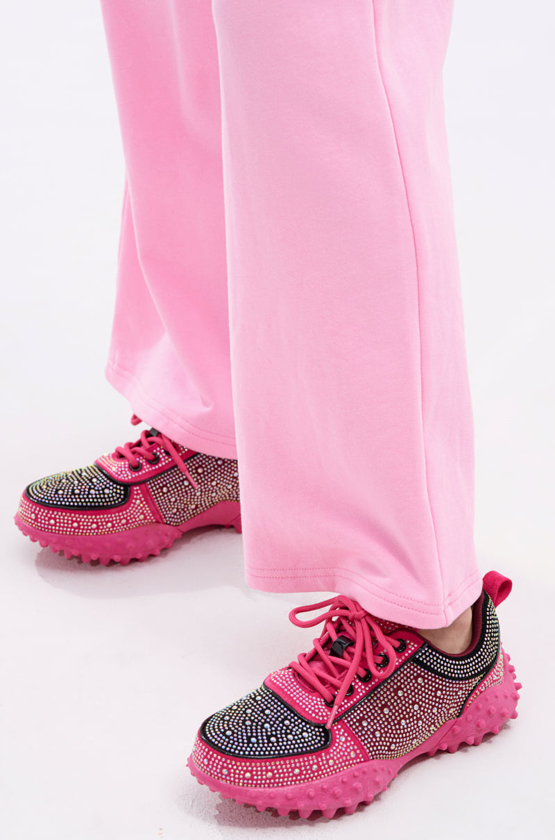 Someone wearing light pink pants and AZALEA WANG ISABEAU FUCHSIA COLOR BLOCKED EMBELLISHED SNEAKERS stands on a white surface.