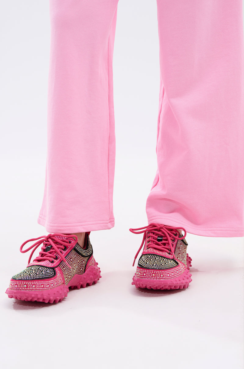 A person wearing loose pink pants and the AZALEA WANG ISABEAU FUCHSIA COLOR BLOCKED EMBELLISHED SNEAKER stands on a white background.