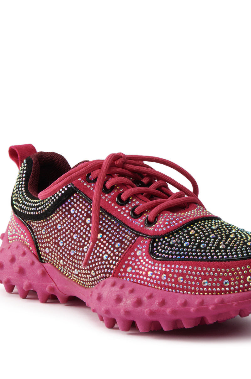 The AZALEA WANG ISABEAU FUCHSIA COLOR BLOCKED EMBELLISHED SNEAKER features vibrant rhinestone detailing, a chunky cleated rubber sole, pink laces, and black accents—ideal for making a statement.