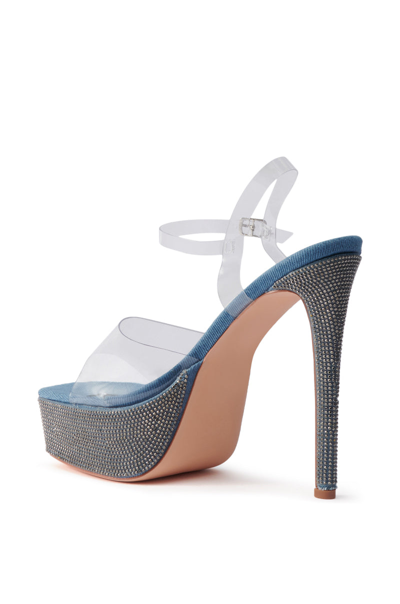The AZALEA WANG ISAURA Denim Platform Rhinestone Sandal features clear straps, an ankle buckle, blue trim, and sparkling rhinestones on the heel and platform. A stiletto heel adds height, while a light tan sole completes the chic design.