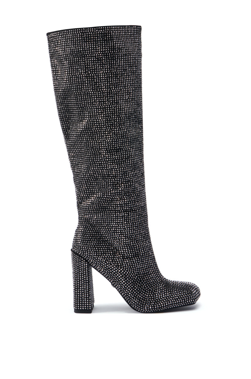 The AZALEA WANG ISKANDER BLACK RHINESTONE BOOT is showcased against a white background, featuring a knee-high design with a chunky high heel. It boasts a texturized and shiny black surface adorned with subtle sparkling rhinestone embellishments, giving it a sleek, tapered appearance. 2