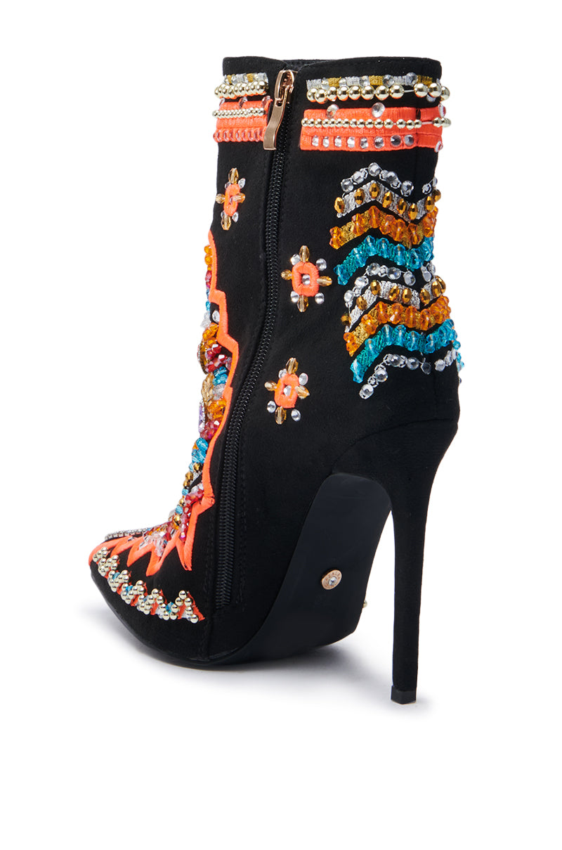 The AZALEA WANG ITSY BITSY MULTI EMBELLISHED BOOTIE is a black high-heeled ankle bootie made from faux suede, featuring detailed beadwork in orange, blue, and gold patterns. It includes a side zipper and a pointed toe, adorned with vibrant floral and zigzag motifs.