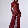 A woman stands against a plain background, wearing a floor-length, sheer floral lace attire with intricate burgundy patterns from the WORK THE ROOM LACE MAXI DRESS collection. The dress elegantly covers her arms and legs while leaving select areas of her torso exposed. She accessorizes with hoop earrings and poses confidently, radiating sophistication and elegance inherent to the Lace Maxi Dress.