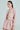 With long hair in a sleek ponytail, they confidently wear the ALINNA EMBELLISHED TWEED BLAZER and a high-waisted sparkling pink textured skirt. The cropped silhouette features rhinestone trim as they pose against a light background with their earrings softly glinting.