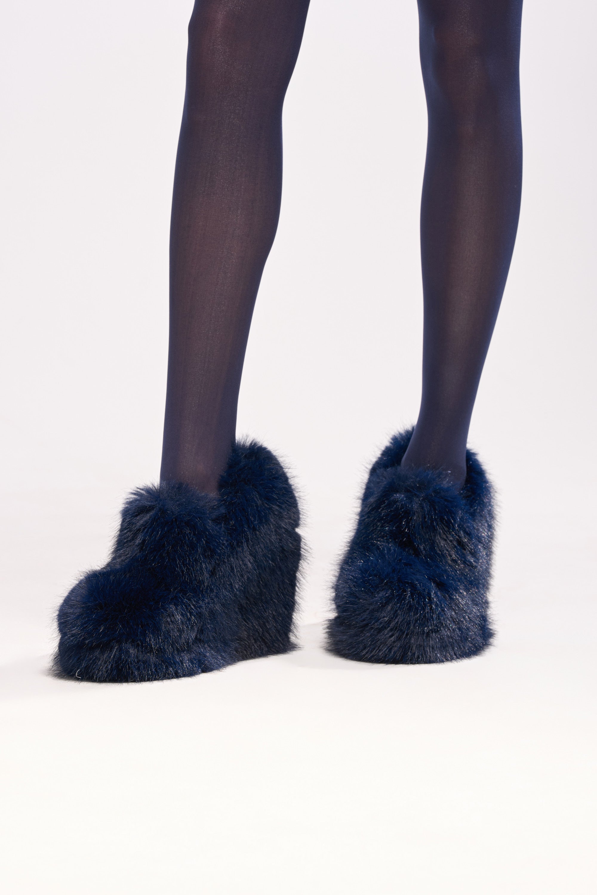 A person wearing dark tights and AZALEA WANG JAEKE NAVY FUR WEDGE PUMP stands on a light surface, showing only their legs and feet against a plain background.