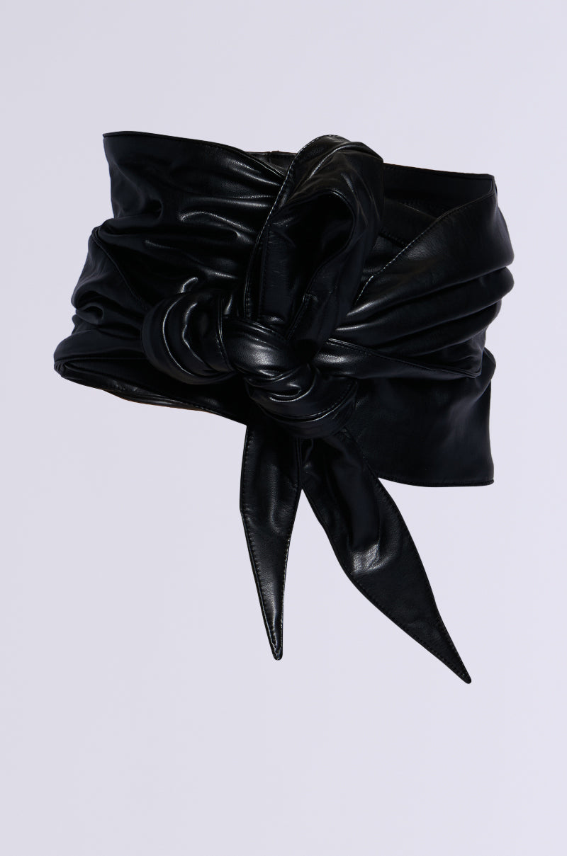 The ESSENTIAL WRAP AROUND TIE BLACK BELT features a wide, knotted front with long, pointed ends. Made from glossy faux leather, it stands out with its sleek and bold design against a plain white background.