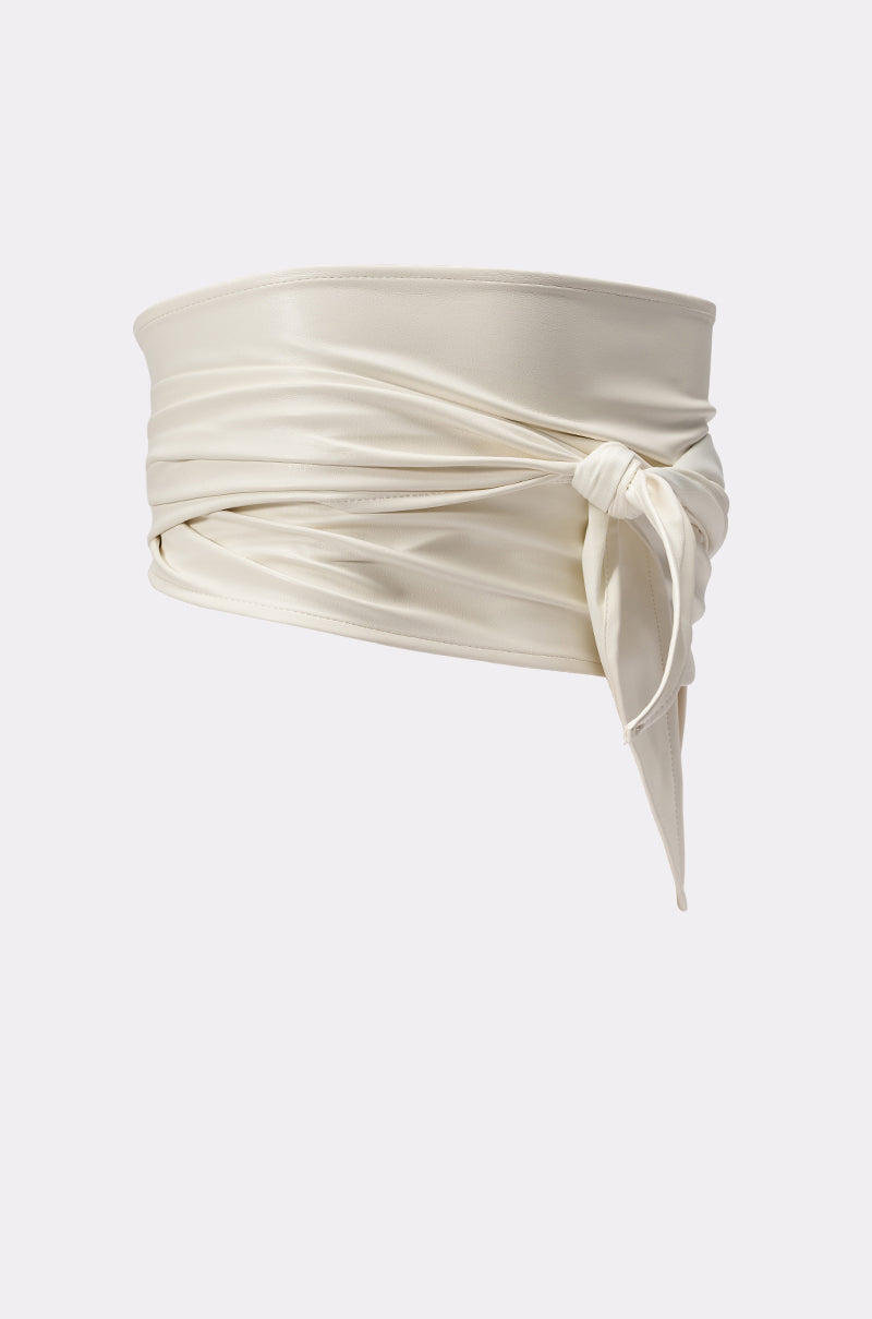 The ULTIMATE CINCH PU BELT is a wide, ivory wrap-around accessory with a smooth, satin-like finish and soft draping folds. Tied at the side, its subtle sheen adds understated elegance against a plain light gray background. 3