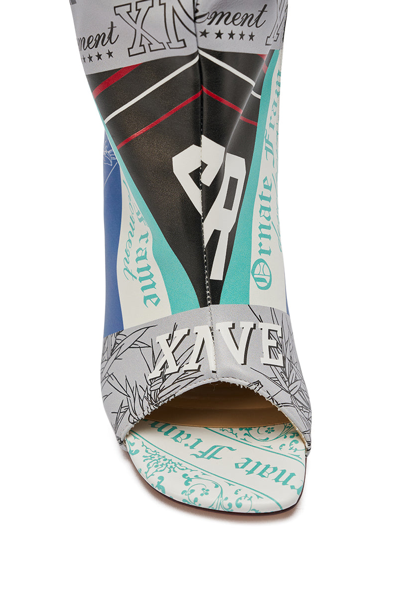 The AZALEA WANG JALISA MULTI NOVELTY PRINTED OPEN TOE BOOT features a stiletto heel and showcases a colorful collage of prints, letters, and patterns in blue, teal, black, and white with visible text elements.