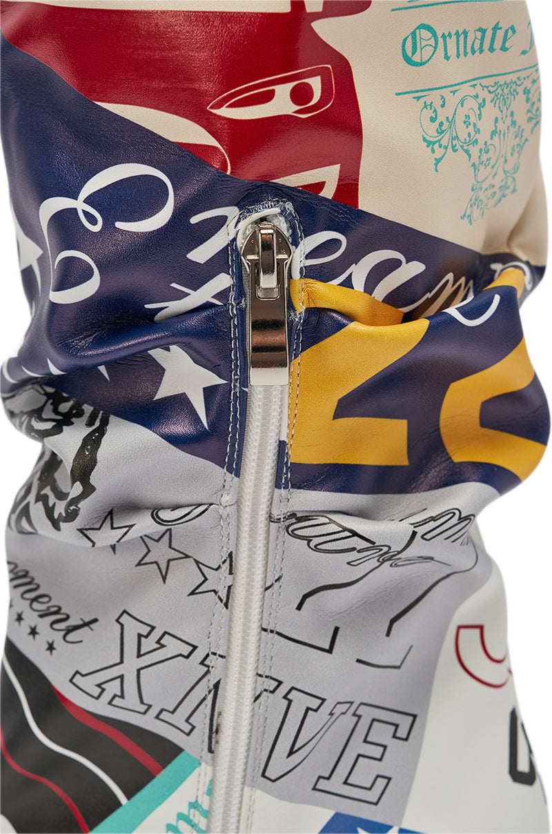 A close-up of the AZALEA WANG JALISA MULTI NOVELTY PRINTED OPEN TOE BOOT featuring a bold mix of blue, yellow, red, black, and teal letters, numbers, and graphics on the knee-high fabric with a central silver zipper.