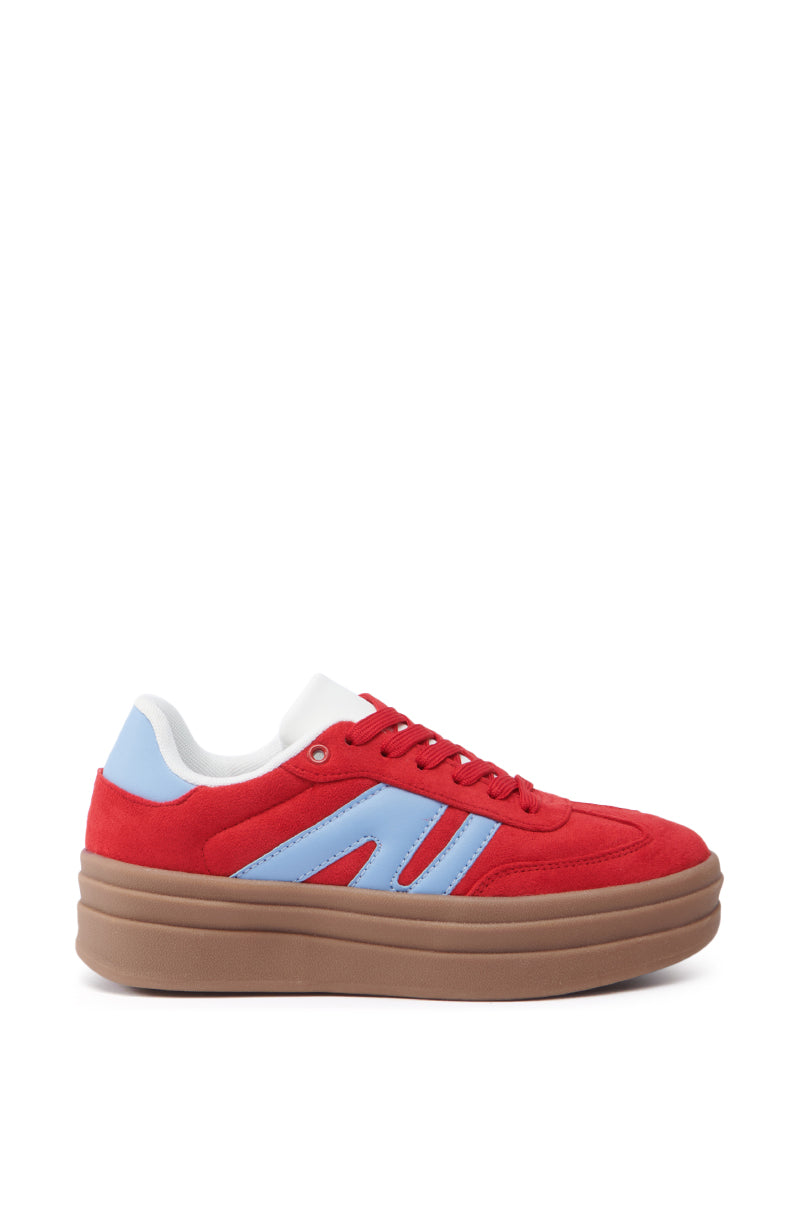 The AZALEA WANG JUMBALAYA RED PLATFORM SNEAKER is a fashionable shoe with red faux suede and blue accents, featuring a thick brown sole. It includes a white interior, red laces, and an almond toe shape, resulting in a vibrant and contemporary look.