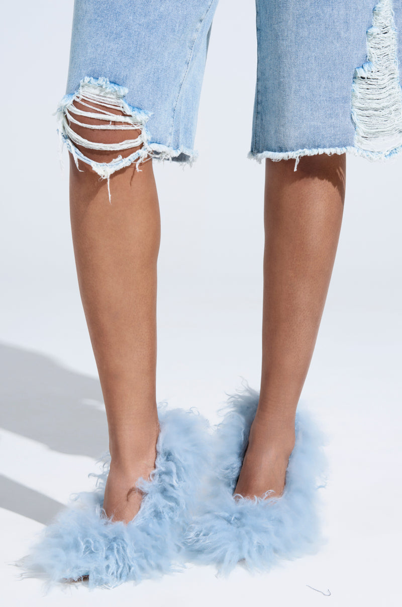 Someone wearing distressed denim shorts and AZALEA WANG JAMEELA BABY BLUE FUR HEELS stands against a light background. The shorts have multiple rips, revealing some skin, while the fluffy fur heels add playful charm to the look.