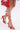 A person wearing the AKIRA JANIKA RED HARDWARE STRAPPY SANDAL in faux leather, paired with a matching red handbag, photographed from mid-thigh down against a plain white background.