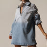 A person confidently wears the COOL GIRL OVERSIZED OMBRE DENIM SHIRT DRESS, featuring a front pocket, paired stylishly with sunglasses, large earrings, and a neck scarf. White knee-high boots complete this casual-cute fashion look against a plain background.