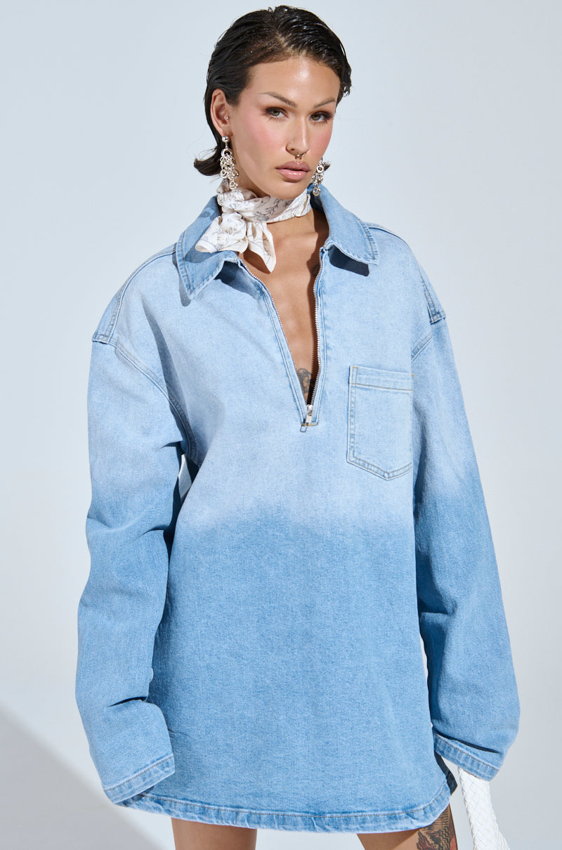 A person in an oversized ombre denim shirt dress with a zipper and pocket poses against a plain background. With short dark hair, large earrings, and a white bandana around their neck, they effortlessly showcase casual-cute fashion in the COOL GIRL OVERSIZED OMBRE DENIM SHIRT DRESS.