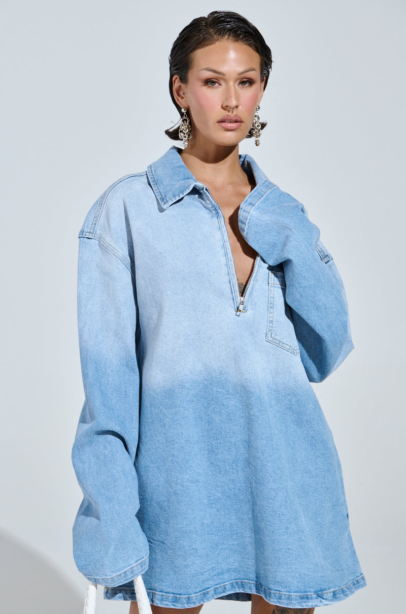 Sporting a COOL GIRL OVERSIZED OMBRE DENIM SHIRT DRESS, complete with long sleeves, collar, and V-neck, this ensemble highlights casual-cute fashion. The short dark hair and large intricate earrings pop against the garment in a plain light gray backdrop.